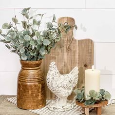 a vase with some flowers in it next to a candle and a chicken on a table