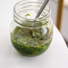 a jar filled with green liquid sitting on top of a white table next to a metal spoon