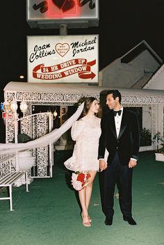 a man and woman standing next to each other in front of a building with a neon sign