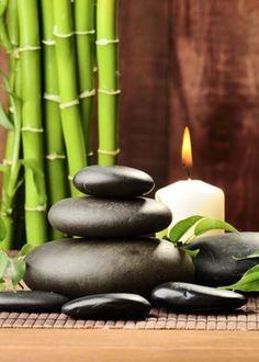 some rocks and candles sitting on top of a wooden table next to bamboo stalks with green leaves