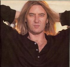 a man with long blonde hair is posing for a photo while wearing a black shirt