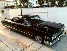 an old black car parked in front of a white fence