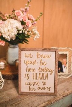 a wooden sign sitting on top of a table next to a vase filled with flowers