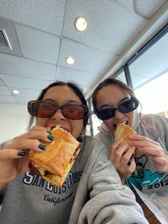 two women are eating sandwiches in an office