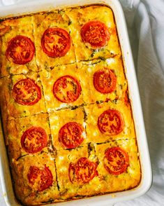 a casserole dish with tomatoes and cheese in it on a white table cloth