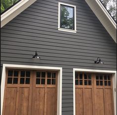 two brown garage doors in front of a gray house with white trim on the windows