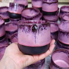 a hand holding a purple cup in front of rows of cups with black rims