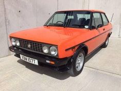 an orange car parked in front of a concrete wall