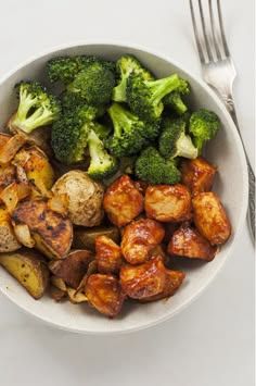 a bowl filled with broccoli and potatoes next to a fork on a table