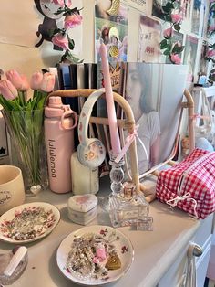 a table topped with plates and vases filled with pink flowers next to pictures on the wall