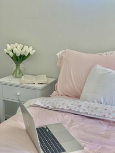 a laptop computer sitting on top of a bed next to pillows and a vase with flowers