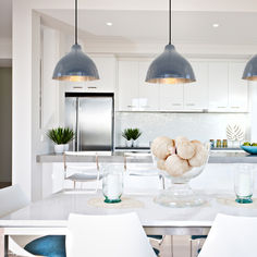 a white kitchen with blue accents and pendant lights hanging over the countertop, along with chairs