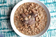 a white bowl filled with beans on top of a blue and white table cloth next to a spoon