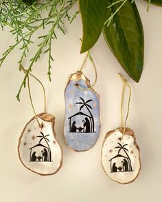 three ceramic ornaments with nativity scene on them hanging from a tree branch and surrounded by greenery