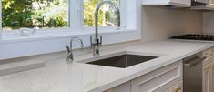 a kitchen with white cabinets and marble counter tops, stainless steel appliances and an open window