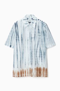 Introducing COS × TABATA SHIBORI, an exclusive collaboration of artworks by artisan Kazuki Tabata that honor the traditional craft of Japanese shibori. The motif on this shirt is achieved using tesuji shibori, a technique wherein fabric is folded, bound by threads and dyed to achieve its signature stripes. Rendered in vivid shades of steel blue and terracotta, it's crafted from a TENCEL™ Lyocell blend that has an effortless drape. Style it with the coordinating pants. Relaxed fitButton closure, side slitsTENCEL™ is a trademark of Lenzing AG. TENCEL™ Lyocell is made from renewable wood sources, using a process that recycles 99% of all chemicals and water  Shell: 83% TENCEL™ Lyocell, 17% Recycled polyester. Excluding trims / Machine wash Back length of size 6 is 31.10" / Model wears a size 6 Blue And Terracotta, Belted Cape, Japanese Shibori, Modern Style Design, Denim Sweater, Cut Sweatshirts, Traditional Crafts, Short Shirts, Dress Trousers