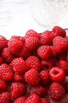 raspberries are sitting on a plate next to a glass vase