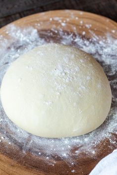 a ball of dough sitting on top of a wooden plate covered in powdered sugar