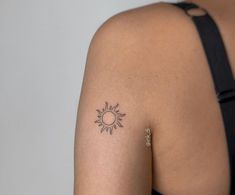 the back of a woman's shoulder with a small sun tattoo on her left arm