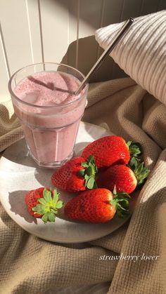 three strawberries on a plate next to a glass of smoothie and some strawberries