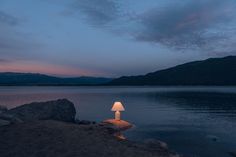 a lamp sitting on top of a rock next to the ocean at night with mountains in the background