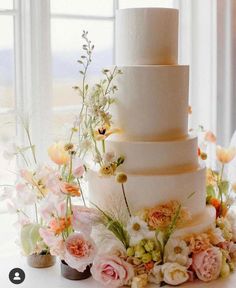 a wedding cake with flowers and greenery on the top is surrounded by other flowers