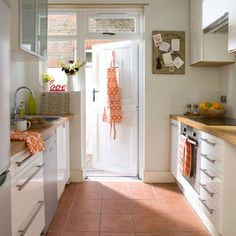 a narrow kitchen with white cabinets and red tile flooring on the walls, along with an open door leading to another room