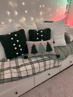 a bed topped with lots of pillows next to a wall covered in christmas lights and string lights