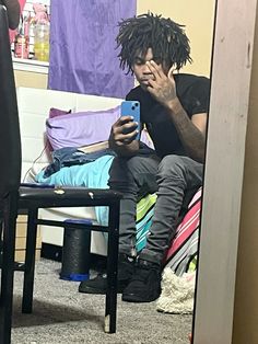 a man with dreadlocks is looking at his cell phone while sitting on a bed