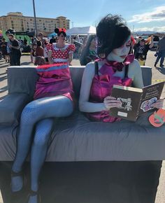 a woman sitting on top of a gray couch next to a man in clown makeup