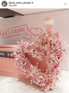 a heart shaped wreath with flowers in front of a pink wall and sign that says welcome to the girl