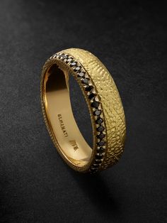 a gold wedding ring with black diamonds on the outside and inside, sitting on a dark surface