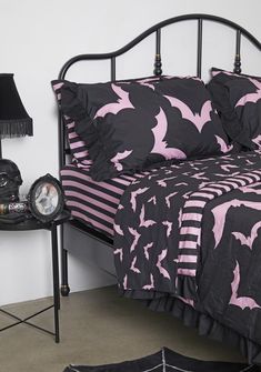 a bed with black and pink comforter next to a night stand on the floor