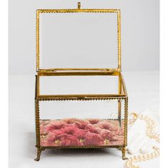 a glass box with pink cushions inside and gold trimmings around the edges, sitting on a white surface