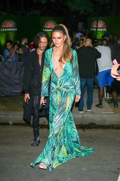 a woman in a green dress is walking down the street with people behind her at night