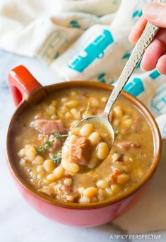 a hand holding a spoon full of soup with meat and beans in it on top of a table