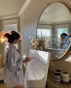 a woman standing in front of a mirror holding an easel