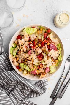 a salad with chicken, lettuce and tomatoes in a bowl next to silverware