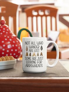 a white coffee mug sitting on top of a table next to a bowl of cookies