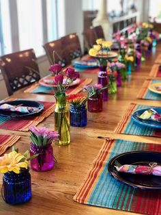 a long table is set with colorful plates and vases filled with flowers on it