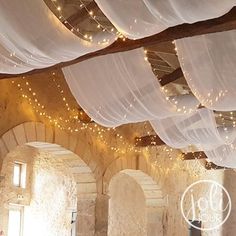 the ceiling is covered with white drapes and fairy lights in an old stone building