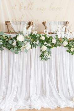 white flowers and greenery decorate the back of a chair at a wedding reception table