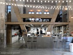 an industrial kitchen with lights strung from the ceiling and two workers preparing food at the counter