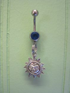 a sun and moon belly ring with a blue stone in the center on a green background