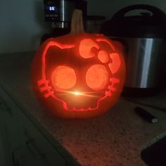 a pumpkin carved to look like a hello kitty face with glowing eyes and ears, sitting on a kitchen counter