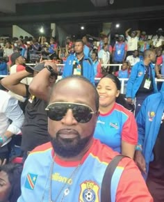 a man with sunglasses on sitting in front of a group of people at a sporting event