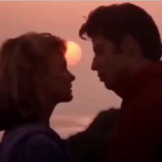 two people standing next to each other with the sun setting in the distance behind them