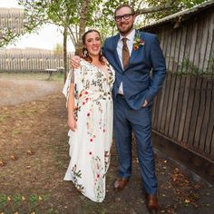 a man and woman standing next to each other in front of a wooden fence with trees