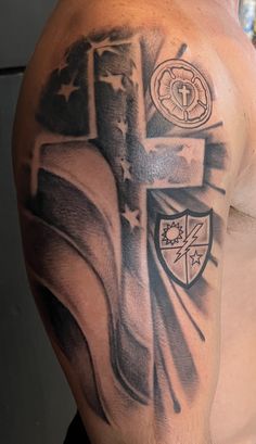 a man with a cross and flag tattoo on his arm is standing in front of a wall