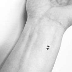 a small black heart tattoo on the left inner arm, with two smaller hearts in the middle